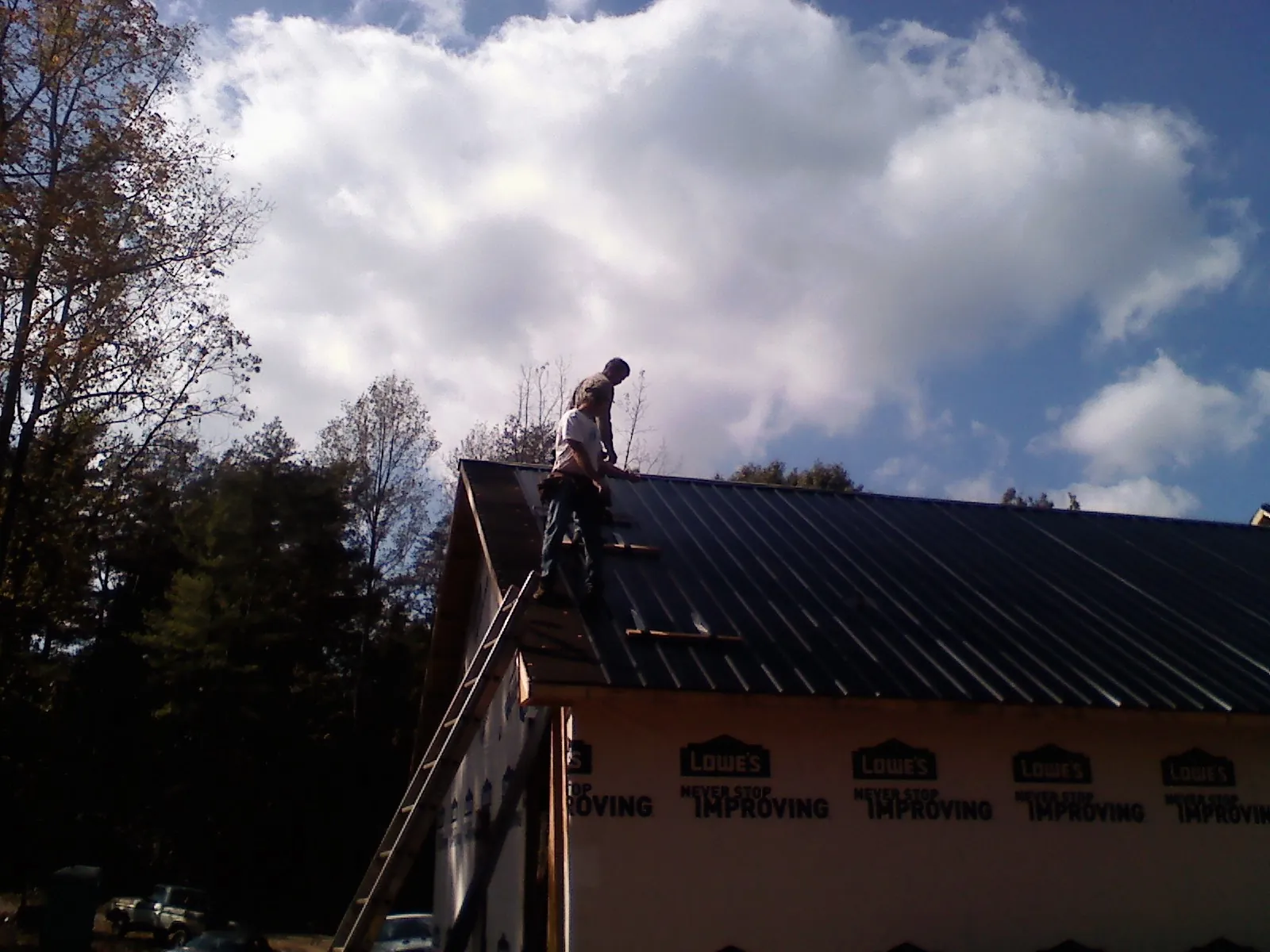 Roofer fastening dark metal panels high against a cloudy sky, from a Roof Inspection job in Bellaire