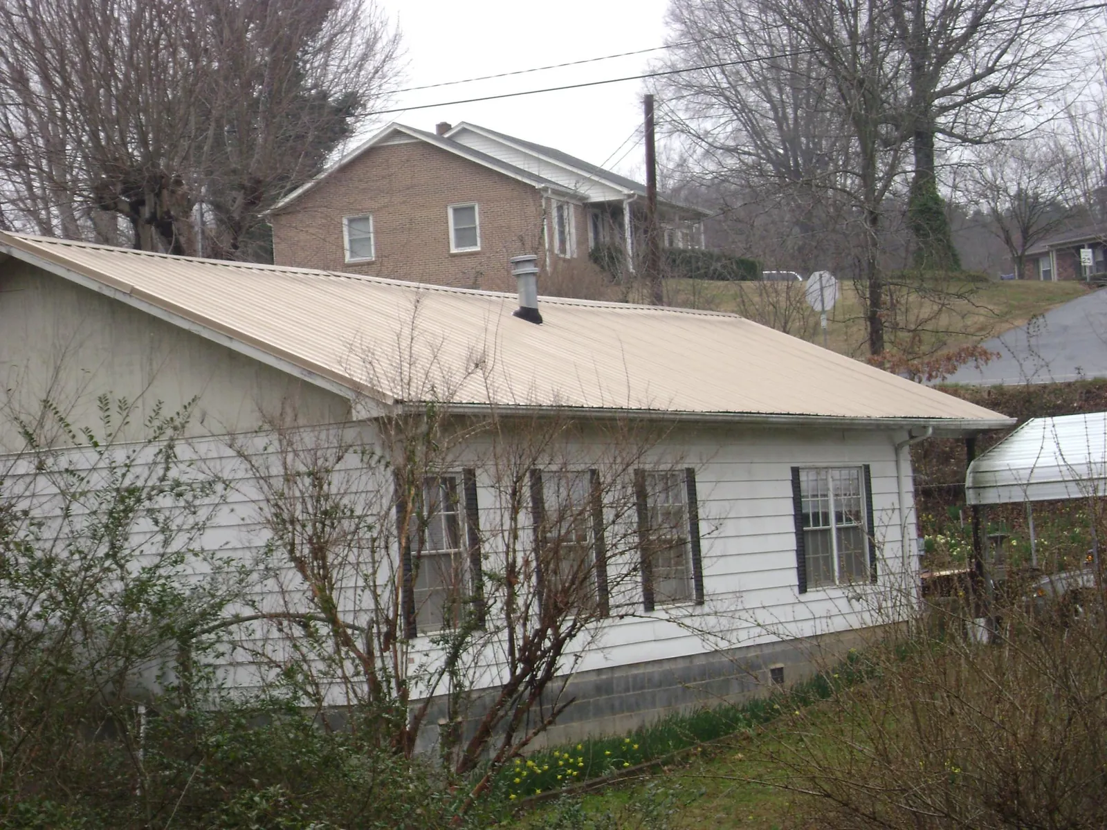 Tan metal roof on a white sided house set into a hillside — Commercial Roofing by Roofing Brothers in Bellaire