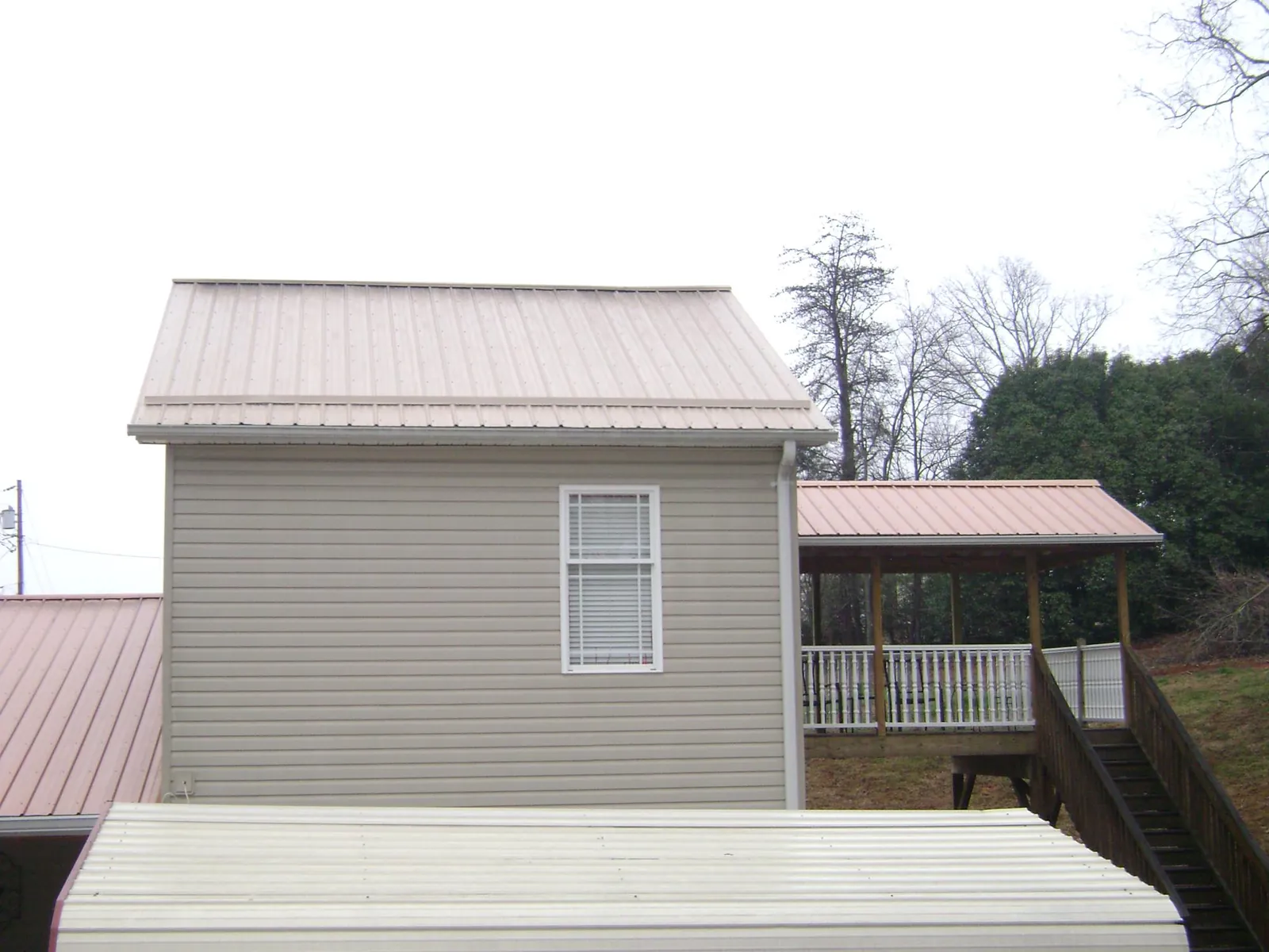Tan metal roofs on a two story addition and attached porch, from a Roof Replacement job in Bellaire